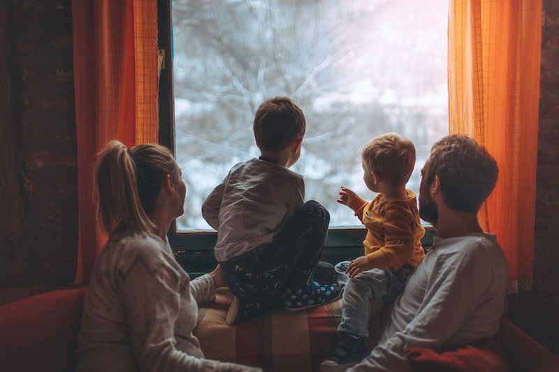 Family inside during winter looking at snowy trees outside. Apex Mechanical blog image.